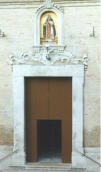Il portale d’ingresso, con la cornice in pietra bianca inornata, è sormontato da un fregio decorativo, anch’esso in pietra bianca scolpita, applicato direttamente sulla parete (foto Tota)